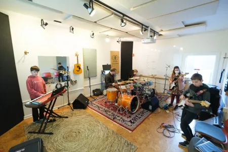 A student band rehearses with keys, drums, and guitars in a Sunburst practice room