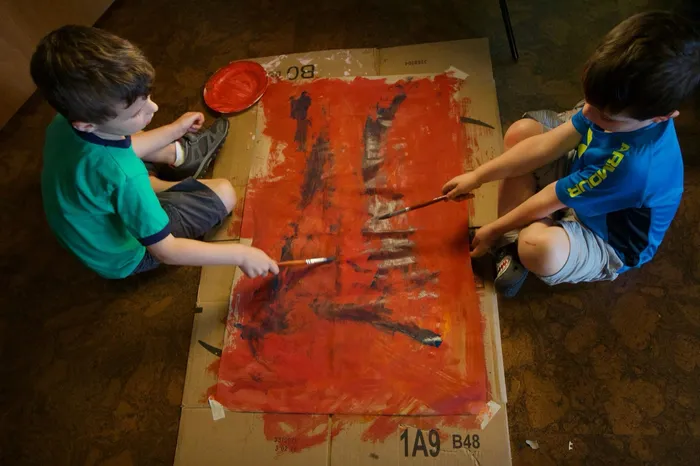 Two campers paint a large red canvas together during an art project
