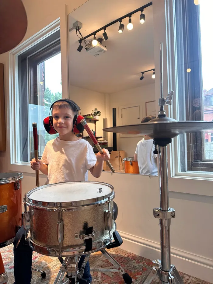 A young camper in headphones smiles from behind a snare drum