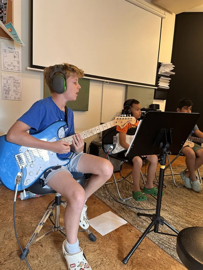 A camper sings while playing electric guitar in a group workshop