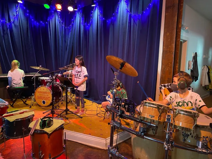 Campers rehearse on stage surrounded by congas, drums, and percussion