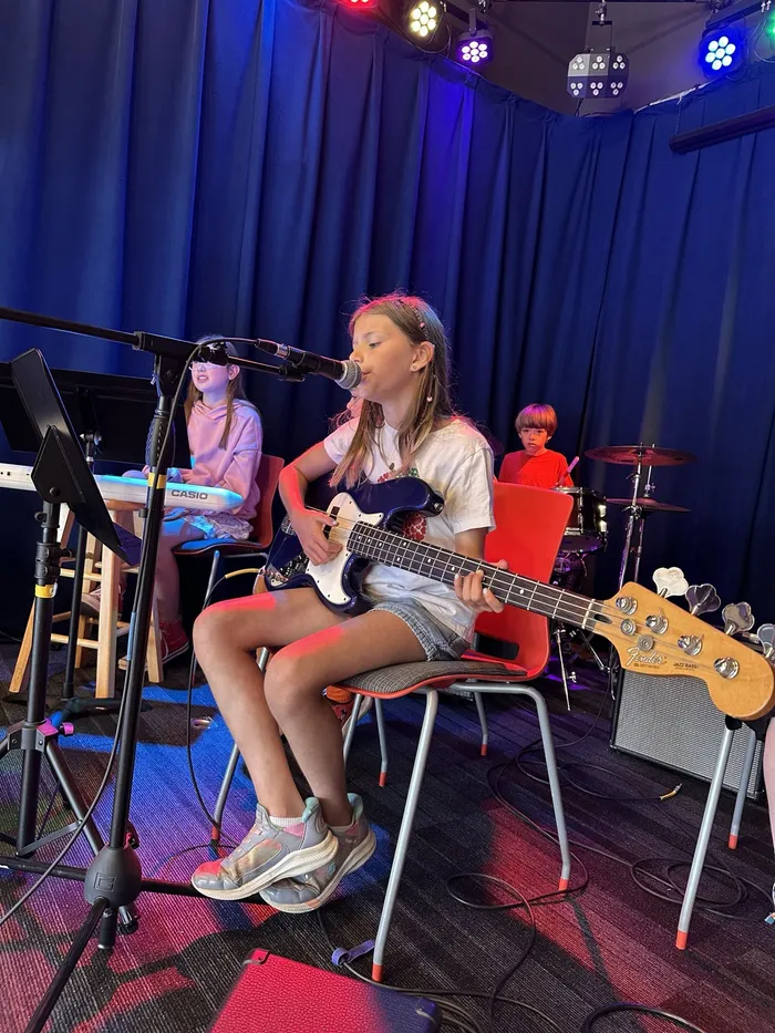 A camper sings and plays bass on stage with keys and drums behind her
