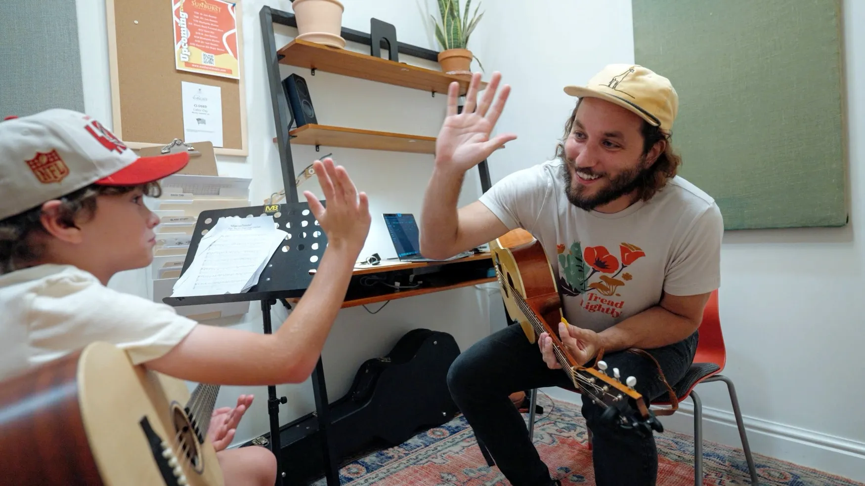 A guitar teacher high-fives a young student during a lesson
