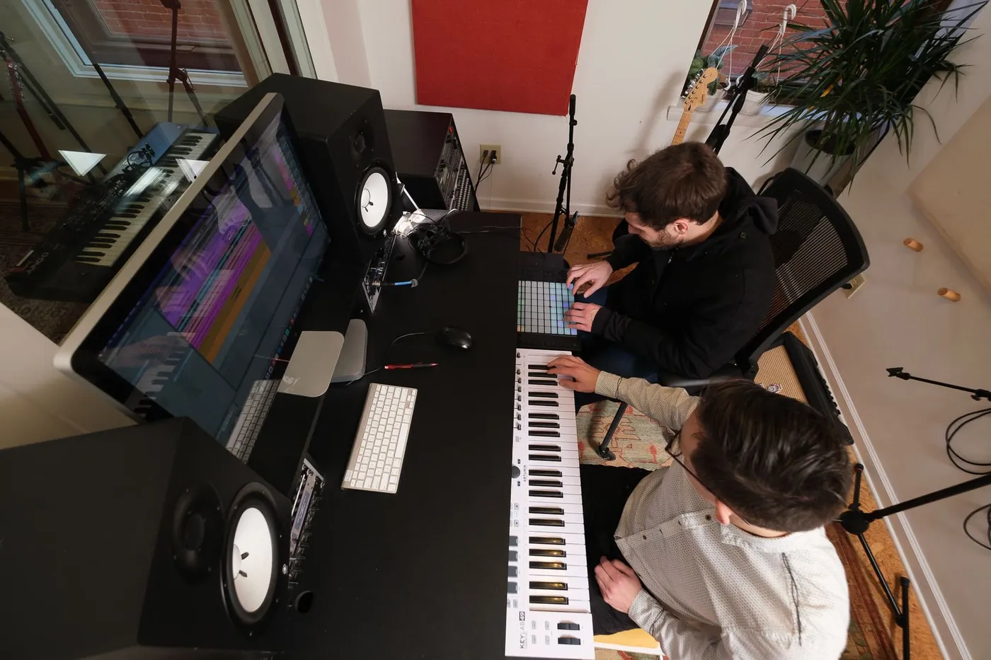 A teacher and student build a track together at a studio desk with keyboards and monitors