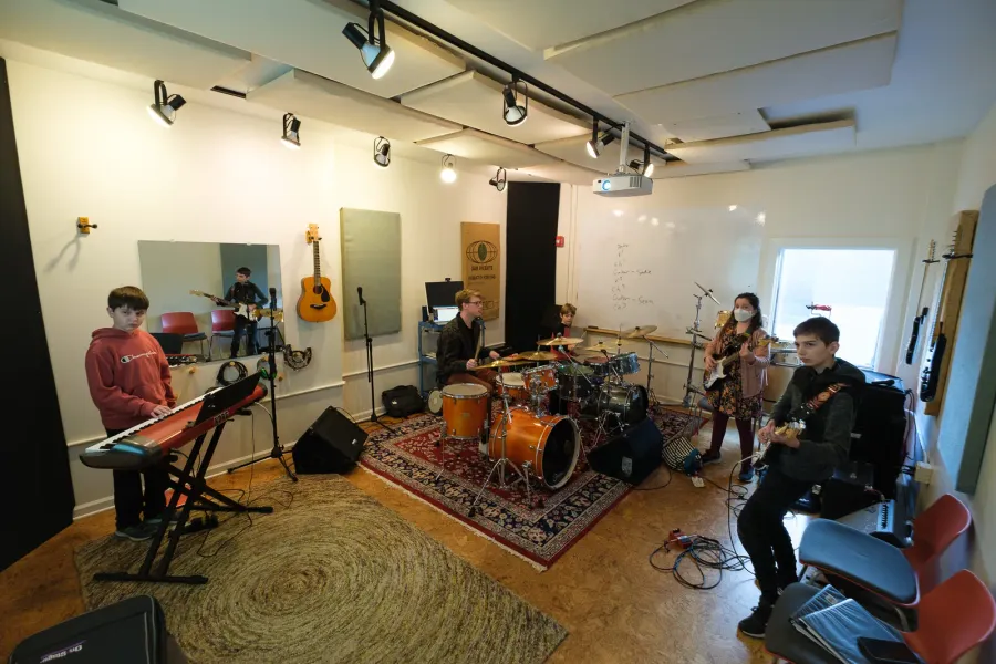 A band of kids rehearses with keys, drums, and guitars in the practice room