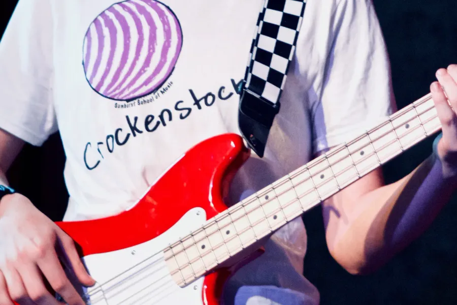Close-up of a student playing a red bass guitar on stage in a Sunburst T-shirt