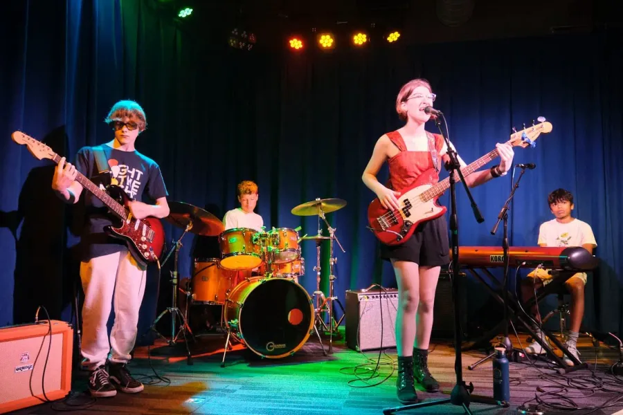 A bassist fronts her band on stage, singing while she plays