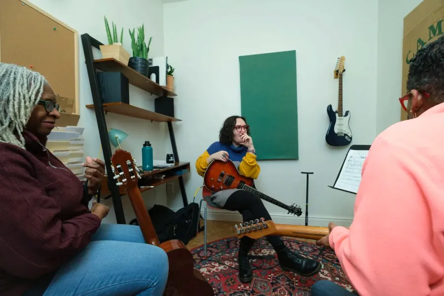 A student with an electric guitar talks through a song with her teacher in a lesson room