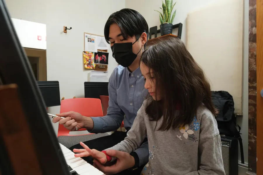 A young student works out a piece at a digital piano with her teacher