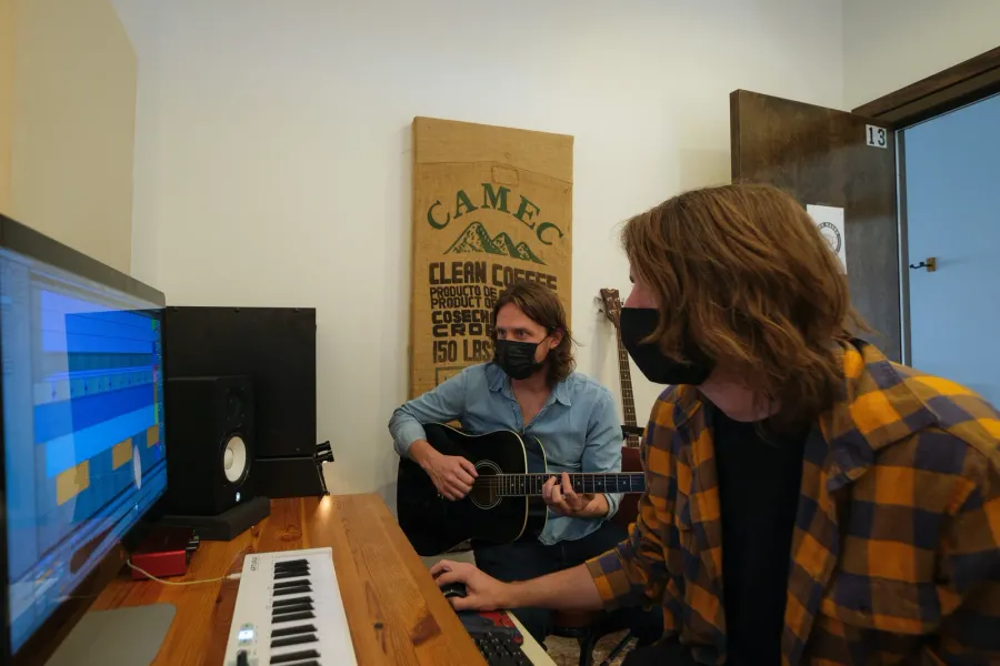 A teacher tracks acoustic guitar while a student runs the session in the DAW
