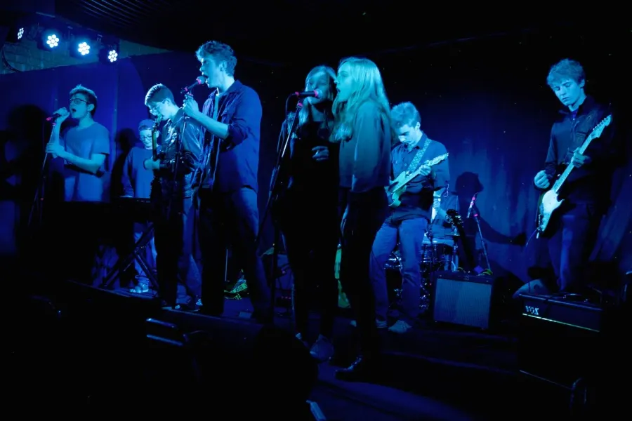 Student singers line the front of the stage under blue lights at a Sunburst show