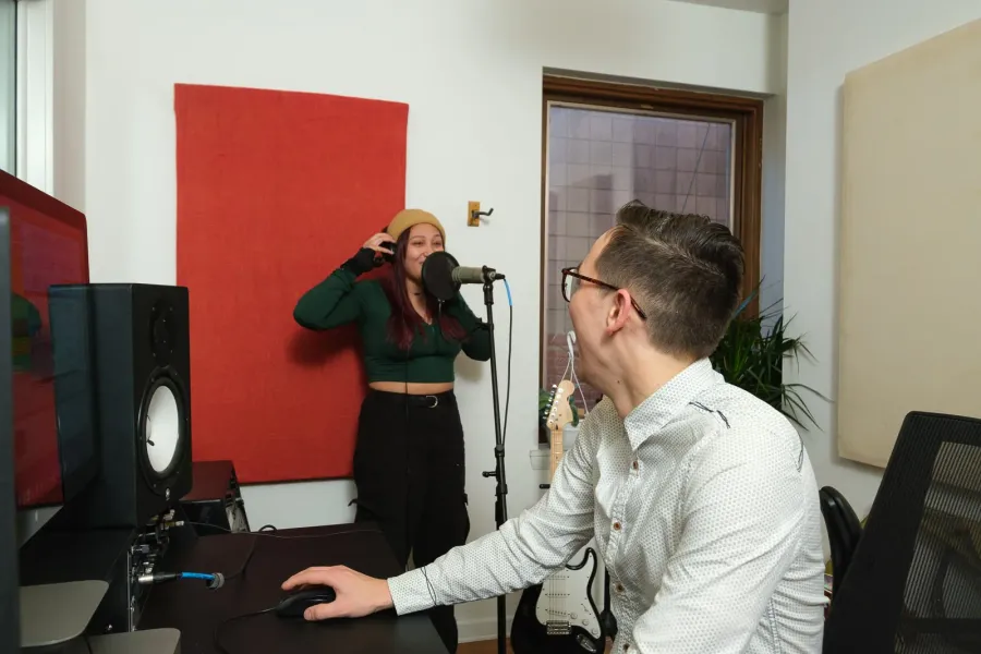 A voice student warms up at the microphone while her teacher works from the studio desk