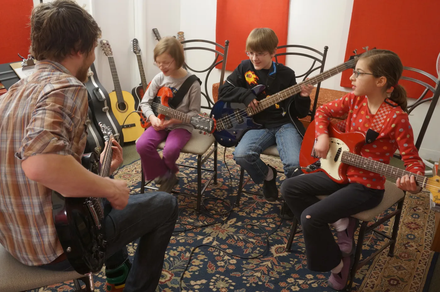 Three young students play electric guitars and bass with their teacher in a Sunburst lesson room